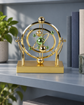 Gold celestial orbit pendulum with green and gold spheres on a shelf beside books
