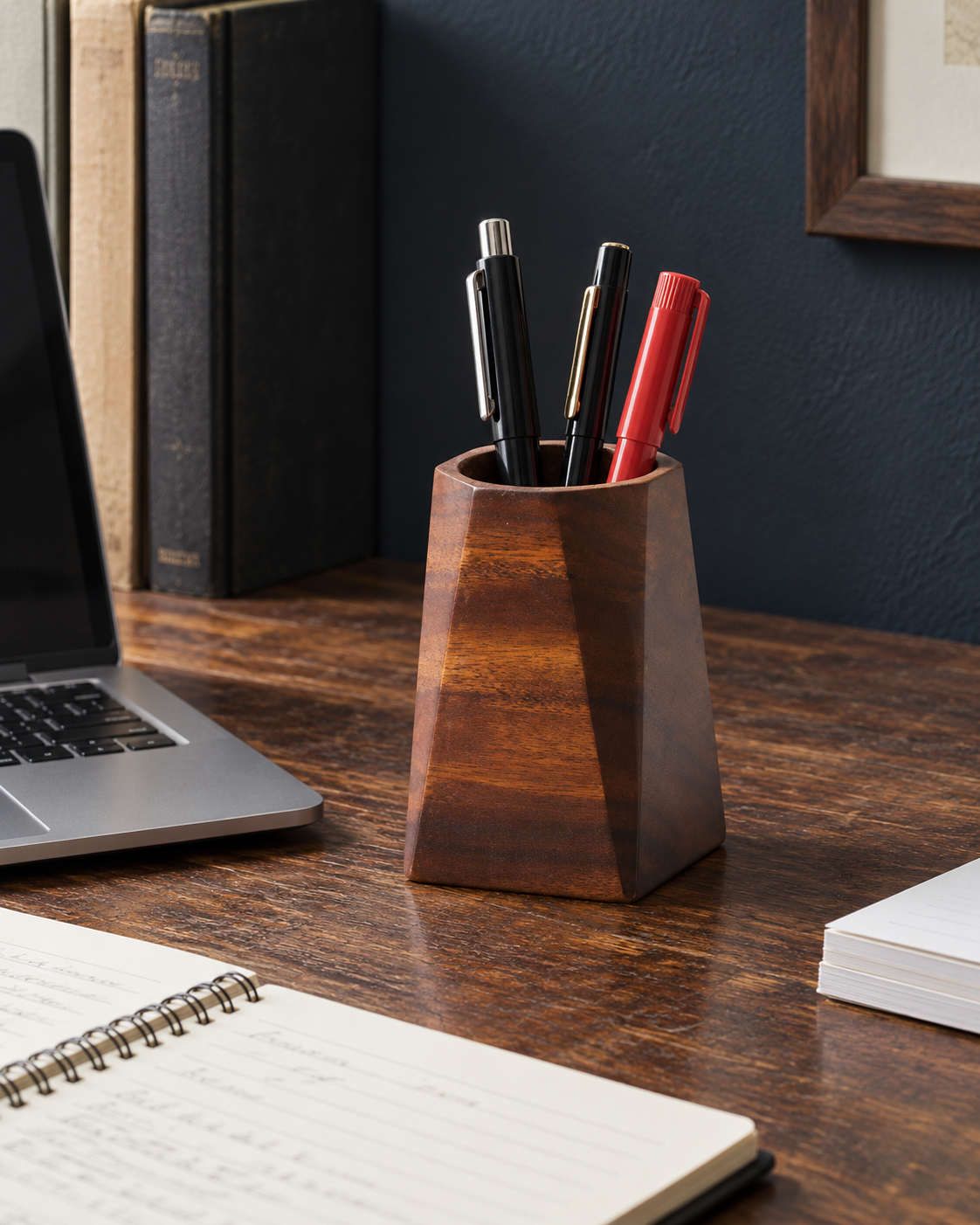 Dark faceted wooden pen holder with pens on a worn desk beside a notebook